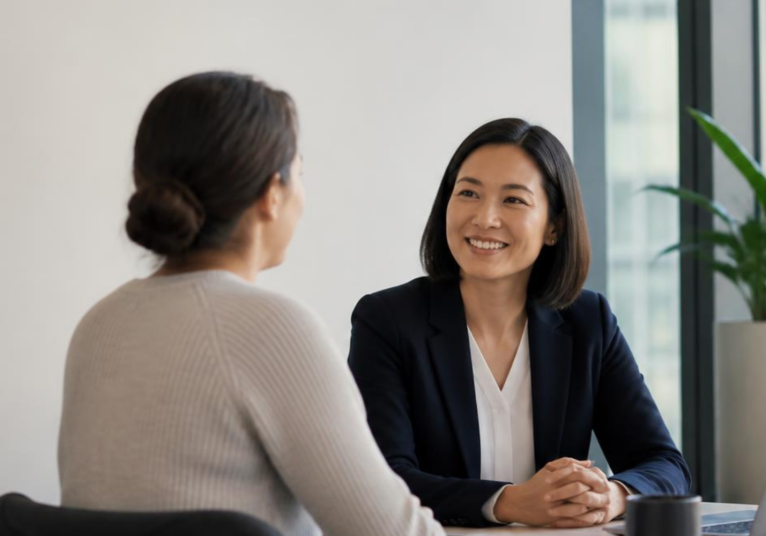 A professional, authentic workplace scene showing a parent returning to work after parental leave, having a supportive conversation with their manager in a modern Australian office